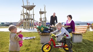 Familie macht Pause auf einem ASFINAG Rastplatz während die Kinder am Spielplatz herumtoben und Fahrradfahren